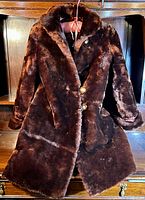 Full view of the brown vintage beaver fur coat on wooden furniture.