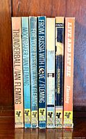 Photo showing the spines of eight vintage James Bond PAN paperback books by Ian Fleming, titles include Thunderball, Moonraker, For Your Eyes Only, From Russia With Love, Goldfinger, and Live and Let Die.