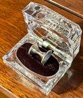 Silver mid century modern ring with textured concave disk feature, sitting inside clear faceted display box with black velvet cushion.