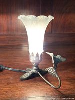 Photo of vintage lamp with frosted glass tulip shade lit up, showing metal hummingbird base