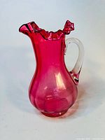 Front view of cranberry glass pitcher showing shape, color, and clear handle