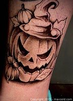 Photo of a tattoo featuring a detailed Halloween jack-o'-lantern wearing a whimsical hat with leaves and smaller pumpkins around it, in black and grey ink.