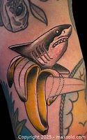 Close-up photo of a colorful tattoo featuring a shark emerging from a peeled banana on skin.
