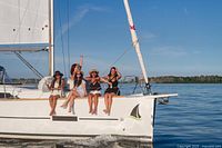 Group of women seated on the edge of a sailboat in sunny weather on the water.