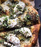 Close-up photo of gourmet food item, possibly a pizza or flatbread topped with greens and dollops of cream.