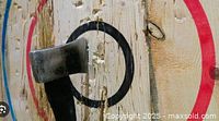 Close-up of wooden axe throwing target with an axe stuck in the black bullseye ring showing wear marks and wood grain detail.
