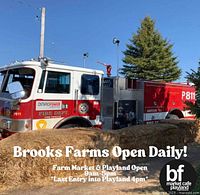 Photo showing a fire truck climber attraction with hay bales and informational sign for Brooks Farms open hours.