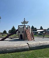 Pirate ship style playground structure with climbing walls, ladders, and a slide on grassy outdoor area with clear sky