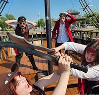 Actors dressed as pirates onboard a pirate ship stage a sword fight, showing the interactive live performance aspect of the event.