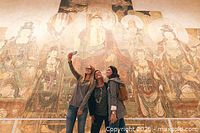 People taking photos and enjoying museum exhibits including large murals and bust sculptures.