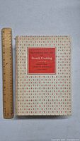 Front cover of the 1961 first edition Mastering the Art of French Cooking with patterned cover and red label.