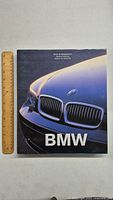 Front cover of the BMW coffee table book showing close-up photo of a blue BMW car grille and headlight.