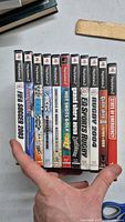 Photo showing the front spines of ten PlayStation 2 game cases held in hand, revealing titles and condition of cases.