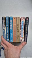Spine view of seven vintage fantasy paperback books in one hand, showing titles and condition.