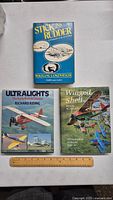 Four vintage hardcover aircraft and aviation books laid out on a table with a ruler for scale.