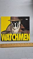 Front cover photo of the Watchmen The Film Companion book featuring the character Rorschach on yellow background with large title text.