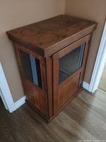 View showing the top, side wood panels and glass windows of the cabinet placed in a corner.