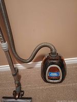 Photo of a Bissell canister vacuum cleaner for hard floors with hose, metal telescoping wand, and handle attached, resting on carpet near wall.