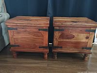 Front view of two wooden end tables with hinged lids closed, showing wood grain and black metal hardware