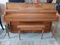 Front view of upright wooden piano with bench on a rug