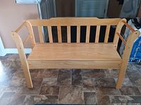 Front view of light wood storage bench with vertical slat backrest and curved armrests