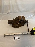Side view of a 3 inch cast iron bench vice showing jaws, screw handle and measuring tape indicating size.
