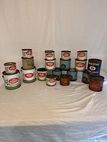 Group of assorted vintage honey tins in various sizes and designs, mostly with lids, arranged on a flat surface against a plain background.