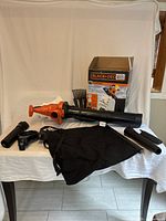 View of the Black & Decker blower/vac/mulcher unit with various attachments and collection bag arranged on table with product box in the background.