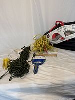 Full view of the items including the Coleman six-person tent in black and red carrying case, green and yellow ropes, wooden hammer, and blue broom and dustpan set.