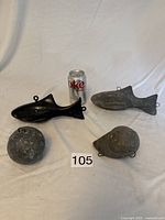 Four led cannon balls for downrigging displayed with a Diet Coke can for scale, two fish-shaped weights and two spherical weights visible.