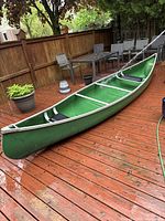 Side-on view of green canoe on deck with aluminium gunwales and three seats visible