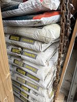 Eight stacked bags of Sakrete Concrete Mix in white packaging with yellow and black print in a storage area.