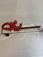 Full side view of the red Homelite corded electric hedge trimmer lying horizontally with attached power cord and blade guard.