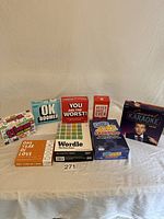 Photo of eight boxed games arranged in a row on a white fabric surface showing titles including OK Boomer, You Are The Worst!, Never Have I Ever, Corporate Karaoke, One Year of Love, Wordle, Did JOKE You?, and 2 Truths 1 Lie.