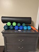 Full view of dumbbells set, yoga mat rolled, and muscle massager laid on dresser