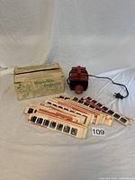 Vintage Magna-Slide projector with multiple colorful Disney slide strips and original box.