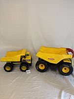 Two yellow Tonka dump trucks side by side on a neutral cloth background.