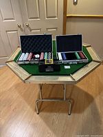 Wide view of poker table showing octagonal wood edge and green felt surface with two open aluminum poker chip cases and automatic card shuffler placed on the table.