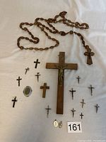 Photo of rosary made from olive pits, large wooden crucifix with Jesus figure, twelve smaller crucifixes, and two religious pendants on white background