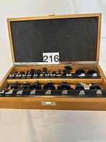 Wood router bits arranged in two rows inside a wooden case with a foam-lined lid.