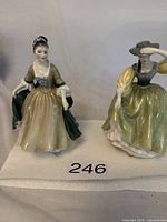 Photo showing two Royal Doulton figurines side by side, Elegance on left in greenish dress and Buttercup on right in yellow-green dress with hat.