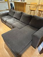 L-shaped four-person couch in smokey blue/grey fabric placed on light wood floor in a room with bar stools and wood paneling.
