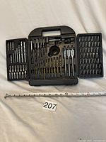 Photo showing open plastic carrying case with assorted drill bits including standard, spade, and masonry bits along with screwdriver bits and adapters organized in molded trays.
