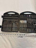 Front view of the open black plastic toolkit showing various drill bits, screwdriver bits, grinding stones, and spade bits organized in molded slots.