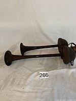 Side view of two long metal air horns with rounded bases on a white cloth surface.