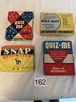 Top-down photo of four vintage card games showing boxes of Quiz Me Numbers, Quiz Me Geography, Snap Card Game, and Lemons Bible Game on a white cloth.