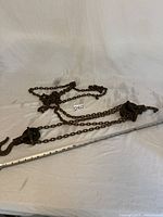 Vintage chain fall with visible metal chain and hooks, measuring approximately 38 inches in length, placed on a white fabric surface.
