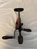 Photo of vintage metal hand drill focusing on crank handle and chuck with visible wear and age marks