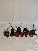 Front view of all vintage oil cans arranged on white paper with varied colors and spout shapes.