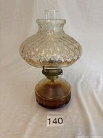 Full view of the vintage oil lamp showing clear textured glass globe, brass burner, amber ribbed glass base, and clear glass chimney.
